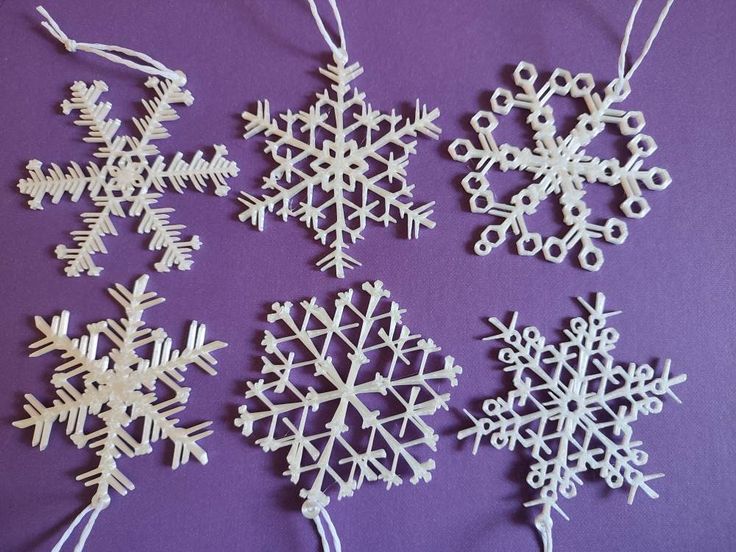 four snowflakes are hanging from strings on a purple surface, one is white and the other is black