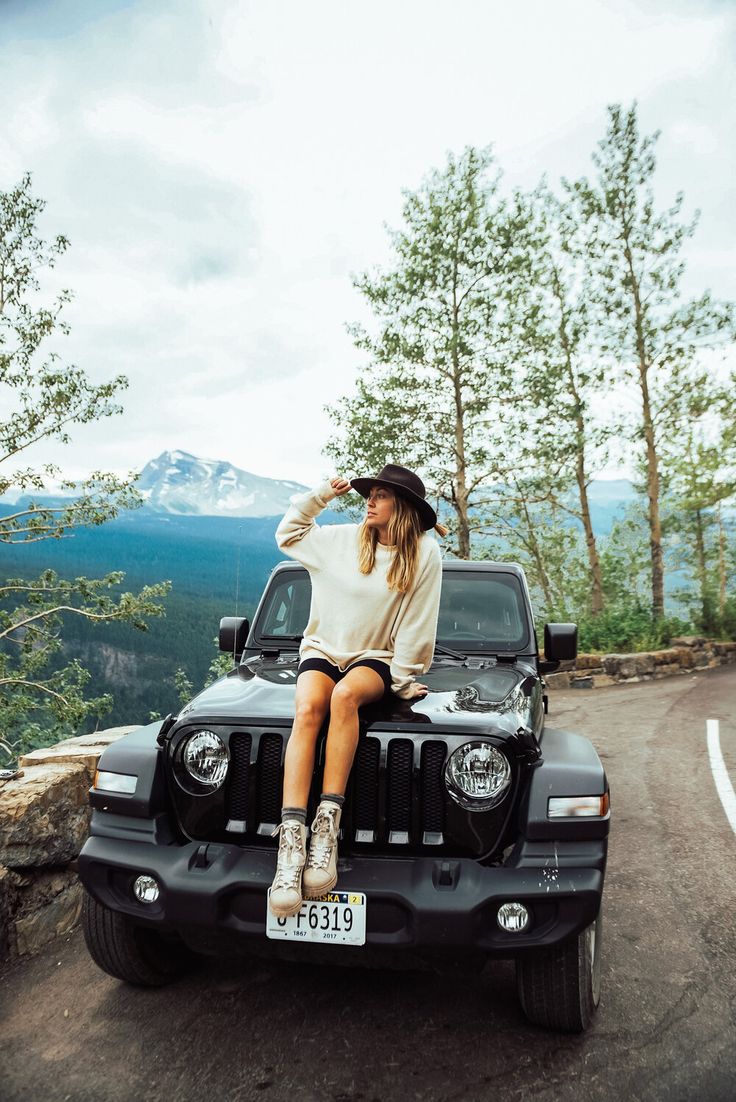 a woman sitting on the hood of a black jeep with mountains in the back ground