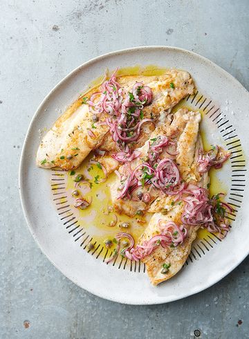 a white plate topped with fish covered in sauce and onions on top of a table