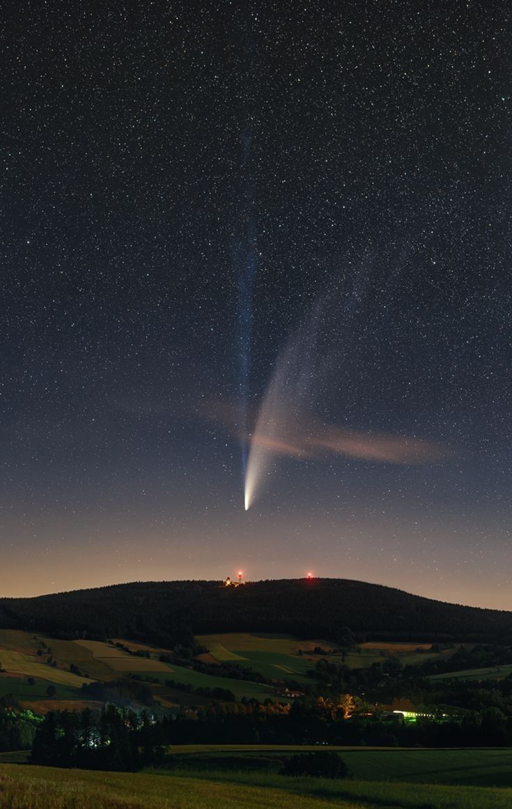 an object is seen in the night sky above a field with trees and hills behind it