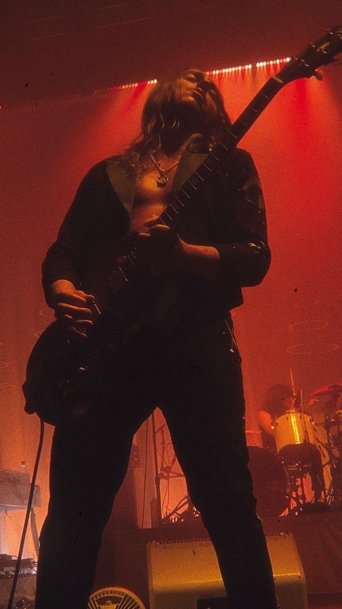 a man standing on top of a stage with a guitar in his hand and lights behind him