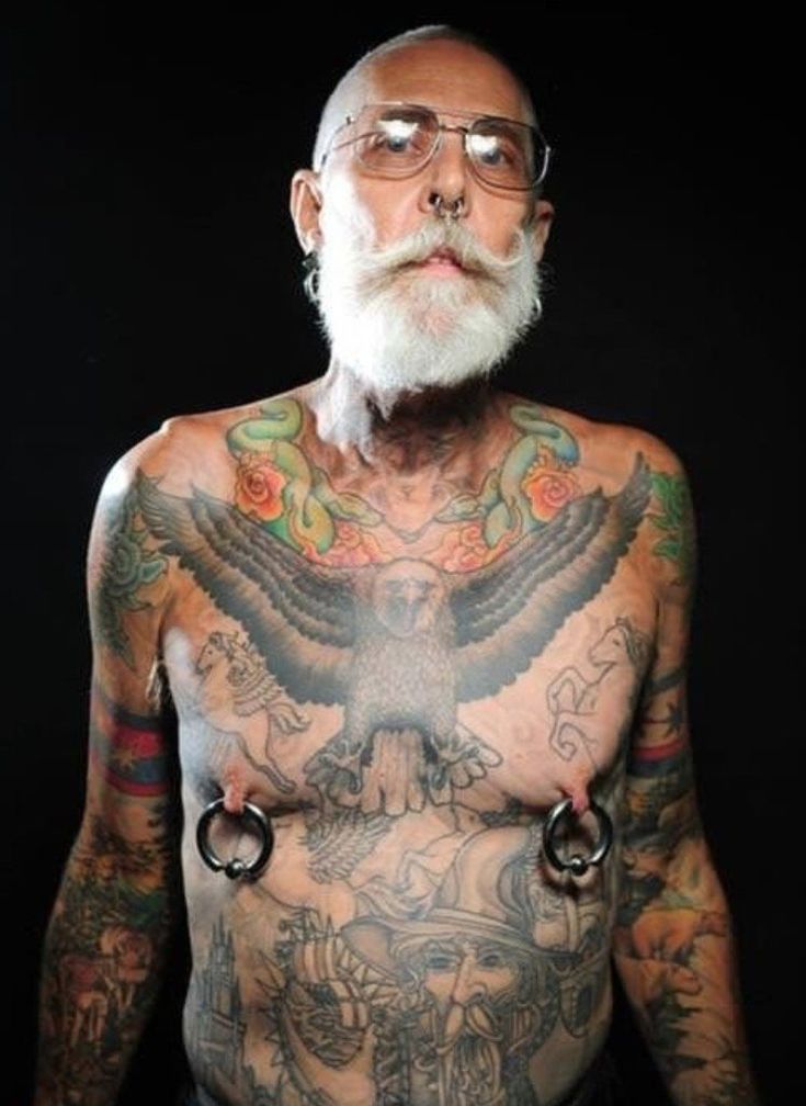 an older man with tattoos and piercings on his chest is standing in front of a black background