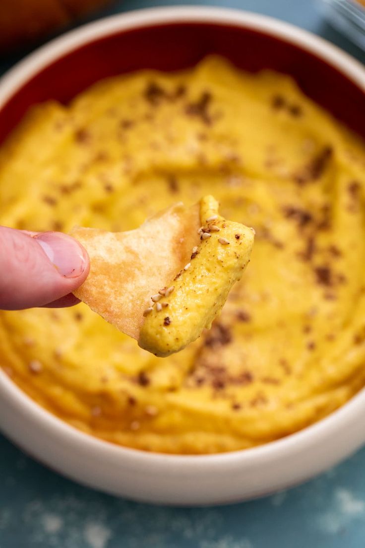 a hand holding a cracker over a bowl of dip