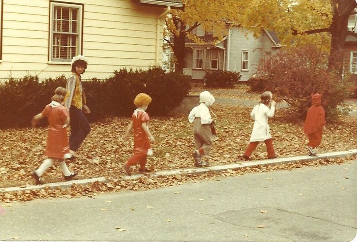 a group of children are walking down the street in front of a house with fall leaves on the ground