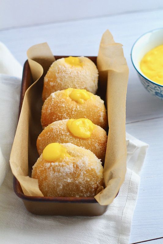 some sugar covered doughnuts in a brown box next to a bowl of soup