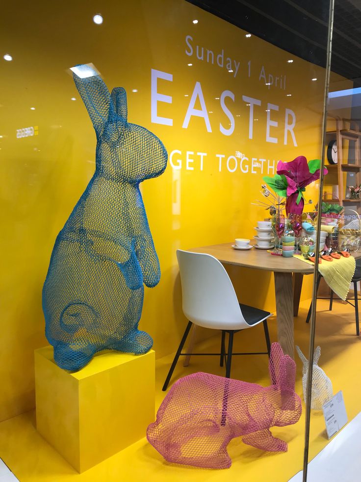 an easter bunny statue sitting on top of a yellow pedestal next to a white chair