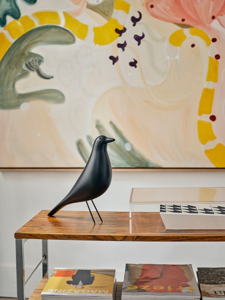 a bird figurine sitting on top of a wooden table in front of a painting