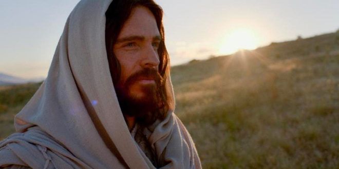 a man with long hair and a beard wearing a shawl in the desert at sunset