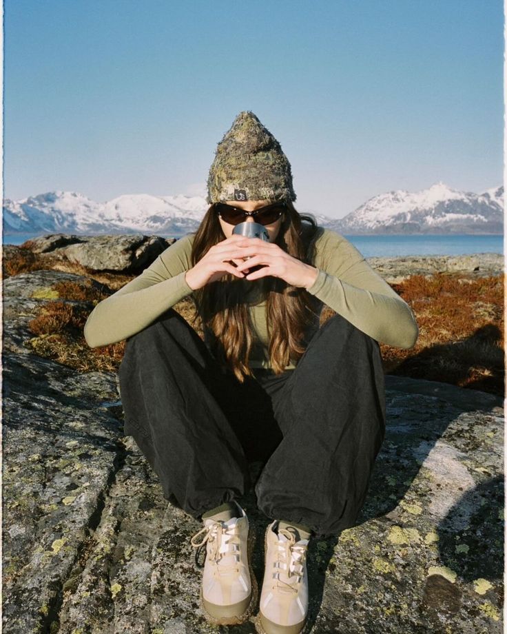 a woman sitting on top of a rock with her hands over her face while wearing hiking gear