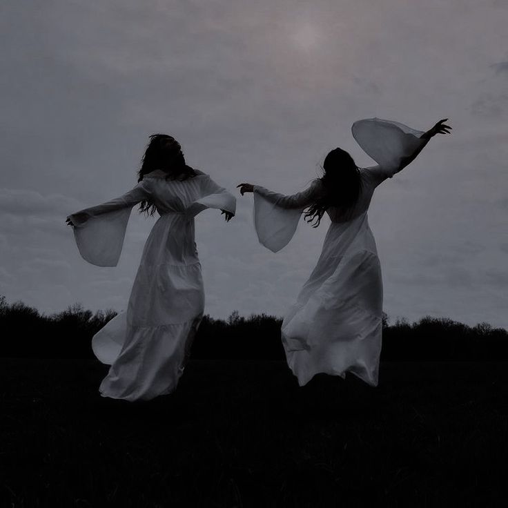 two women in white dresses are dancing on the grass with their arms spread wide open