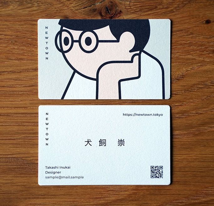 two business cards sitting on top of a wooden table next to each other, one with a man's face drawn on it