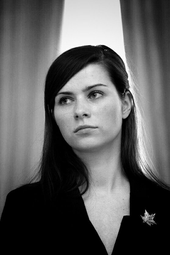 a woman with long hair wearing a black suit and gold star brooch on her lapel