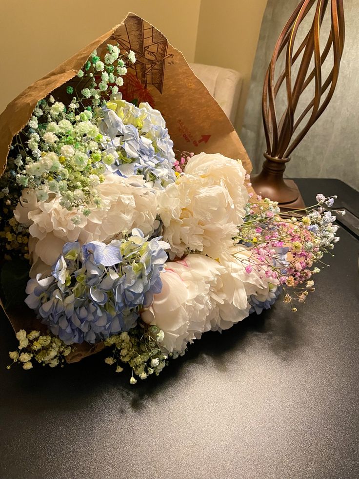 a bouquet of white and blue flowers sitting on top of a black table next to a lamp