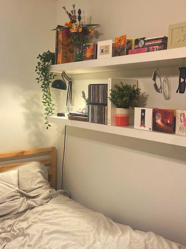 a bed sitting under a window next to a shelf filled with books and plants on top of it