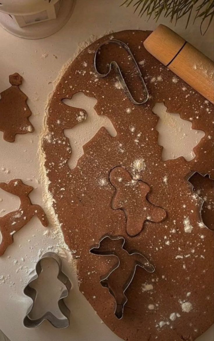 cookie cutters and gingerbread cookies on a white table with christmas decorations in the background