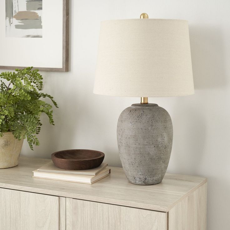 a table lamp sitting on top of a wooden dresser next to a potted plant