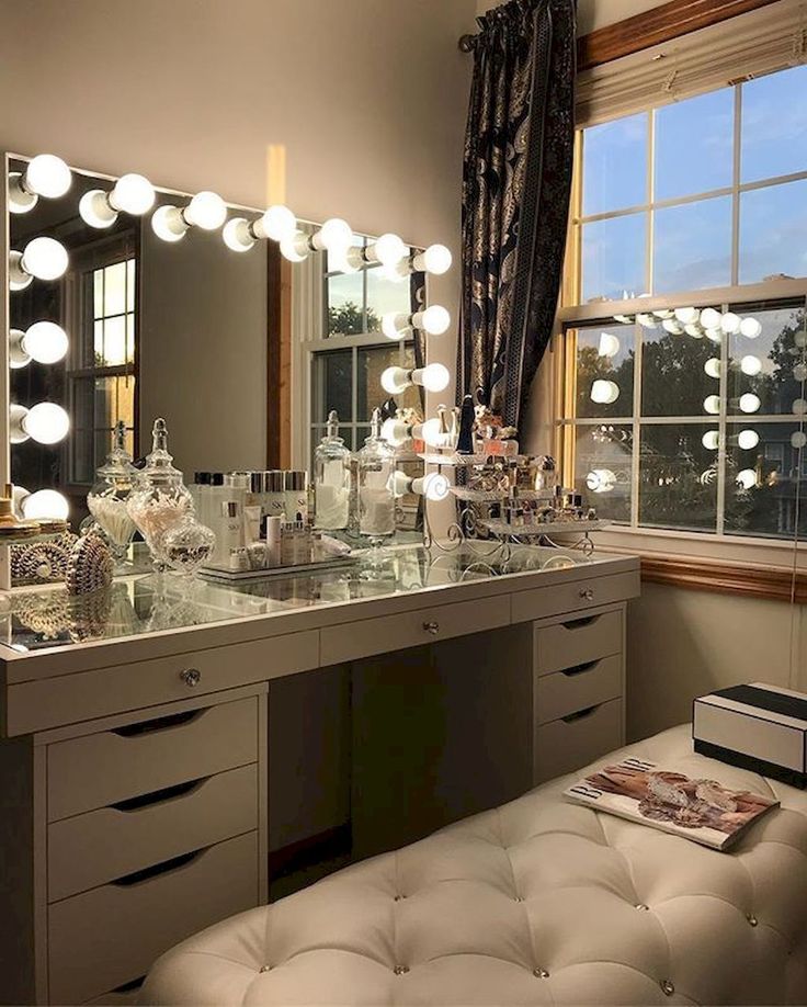 a large vanity with lighted bulbs on the top and drawers in front of it, along with an ottoman