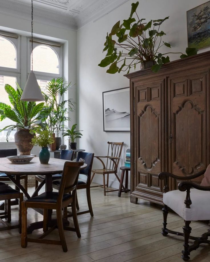 a dining room table surrounded by chairs and potted plants