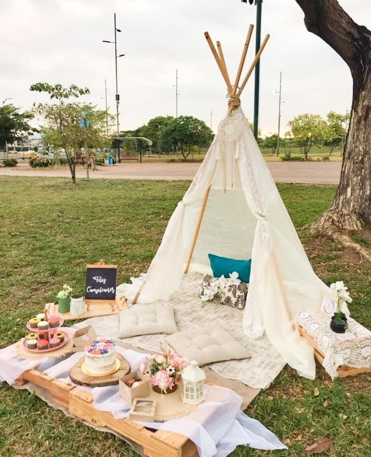 a teepee is set up in the grass with cakes and cupcakes on it