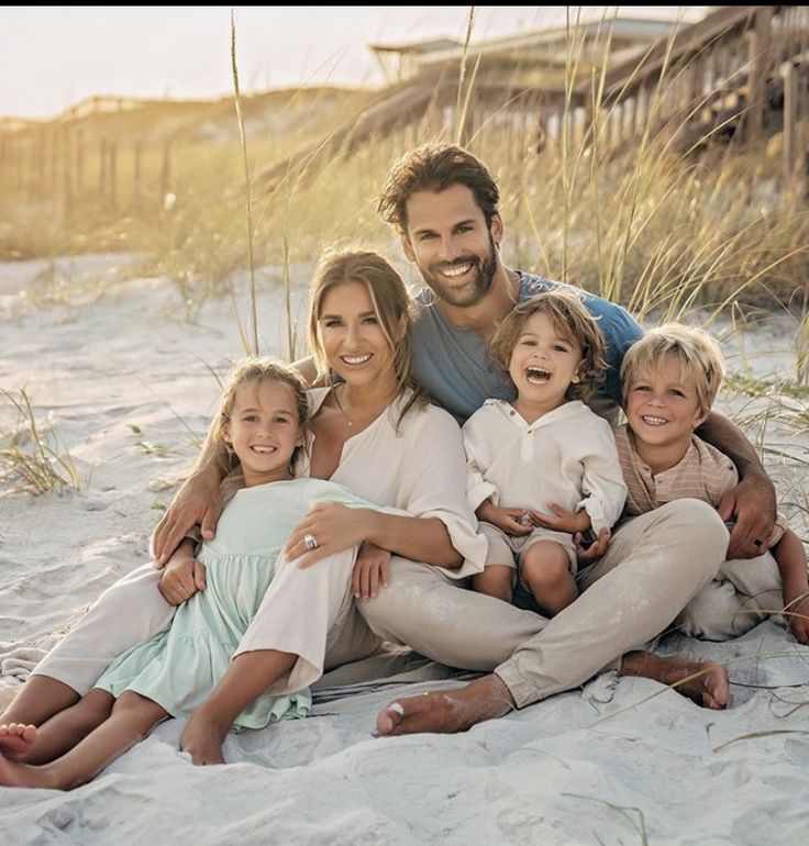 a family sitting on the beach in front of some tall grass