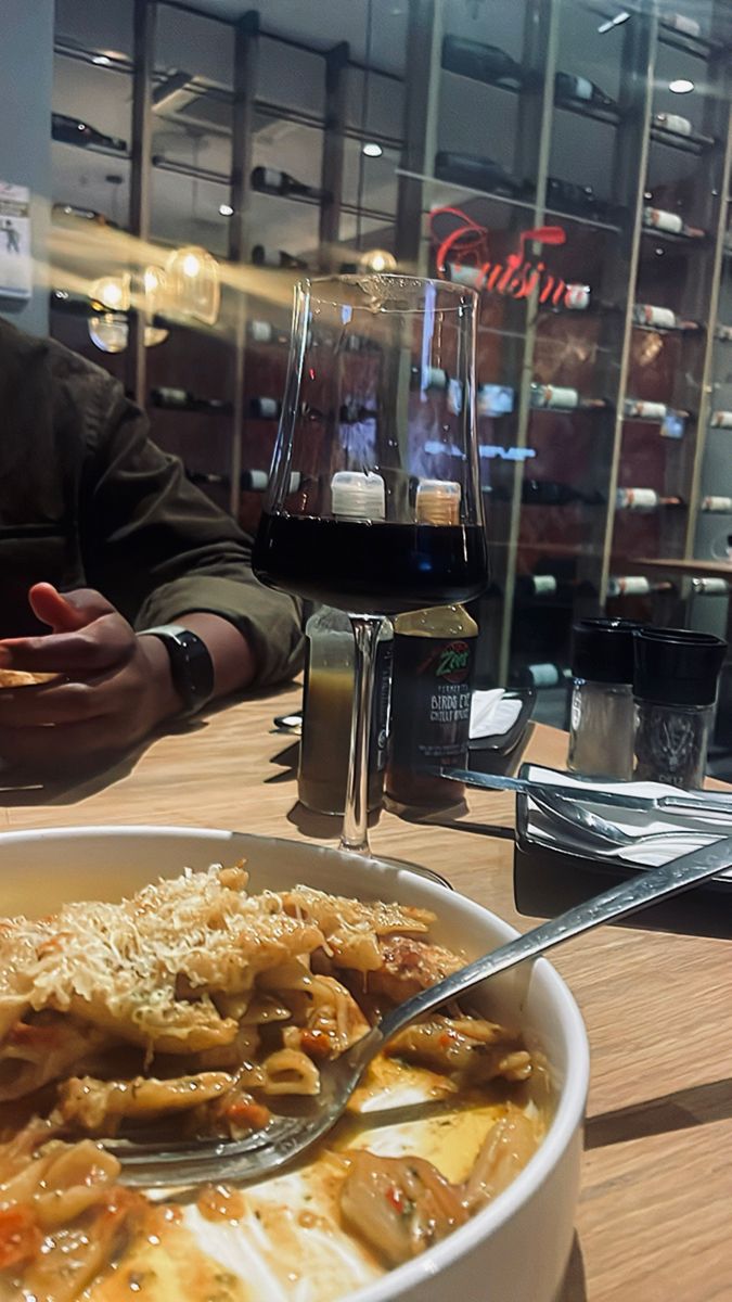 a person sitting at a table with a bowl of food and a glass of wine