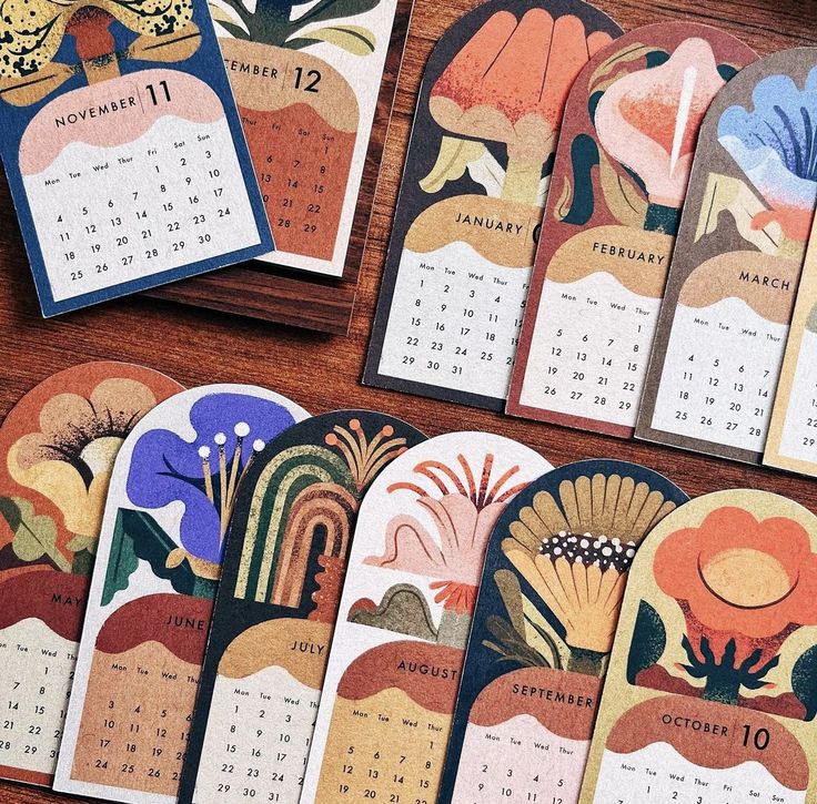 several calendars with colorful designs on them sitting on a wooden table next to each other