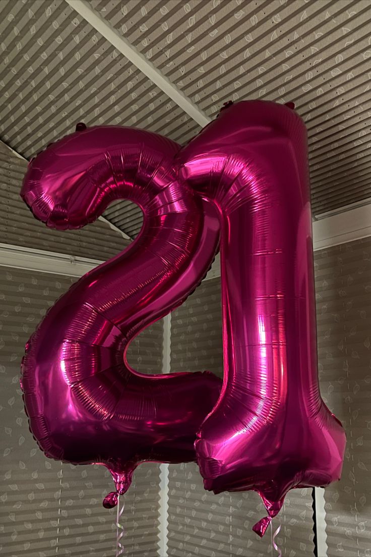 the letter s is made out of shiny pink foil balloons and hanging from a ceiling