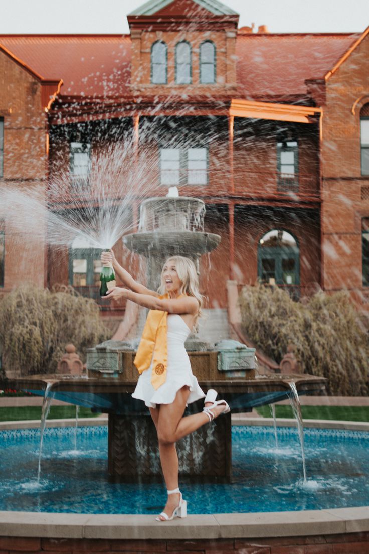 a woman standing in front of a fountain spraying water on her face and holding a beer