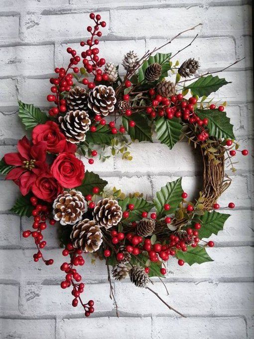 a wreath with pine cones, holly and red berries is hanging on a brick wall