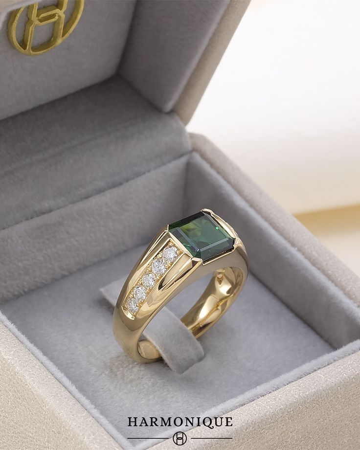 a gold ring with an emerald and diamond set in it's presentation box on display