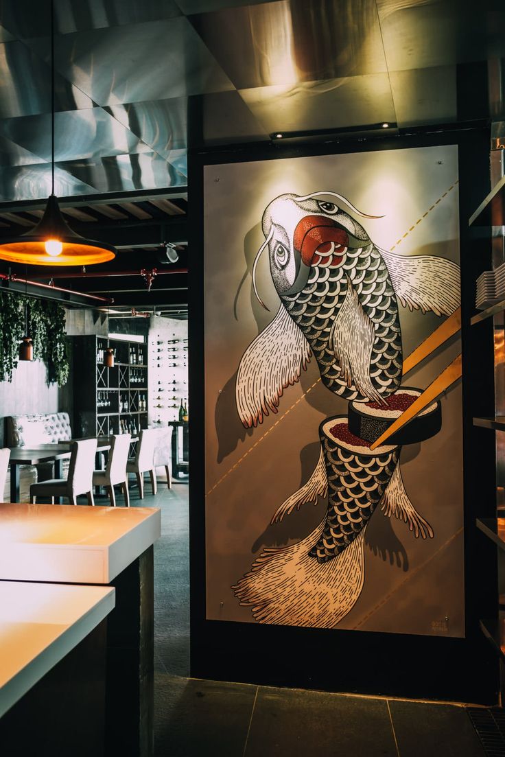 a fish painting hanging on the side of a wall in a room with chairs and tables