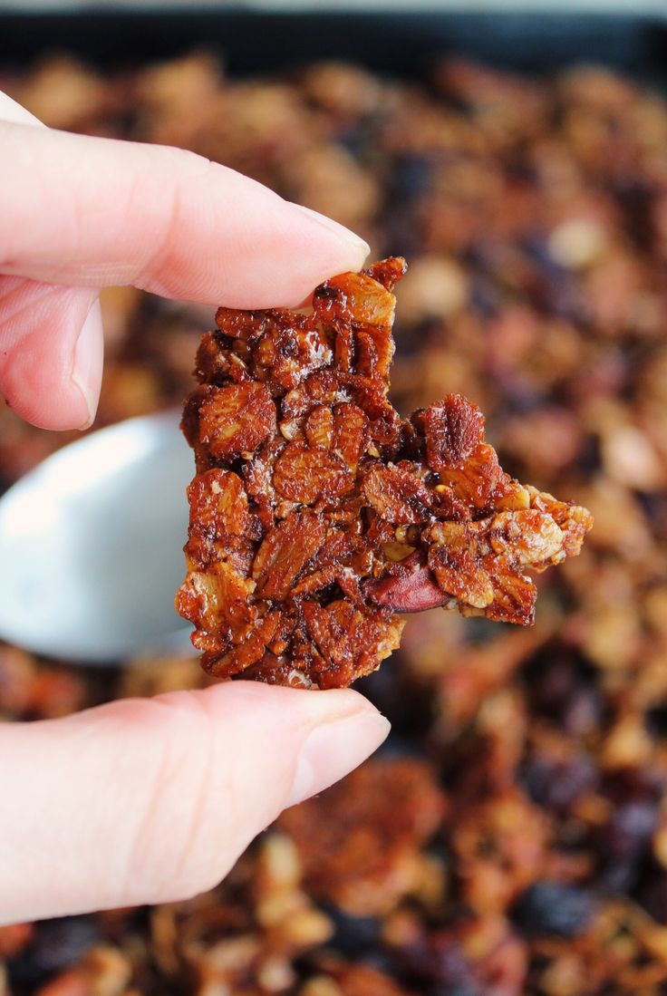 a hand holding up a piece of granola in front of a pan filled with raisins