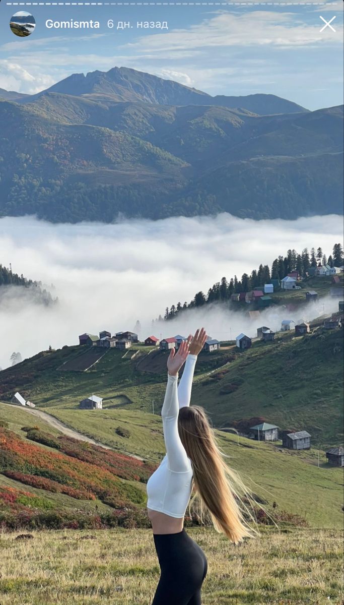 a woman doing yoga in the mountains with her hands up to the sky and clouds behind her