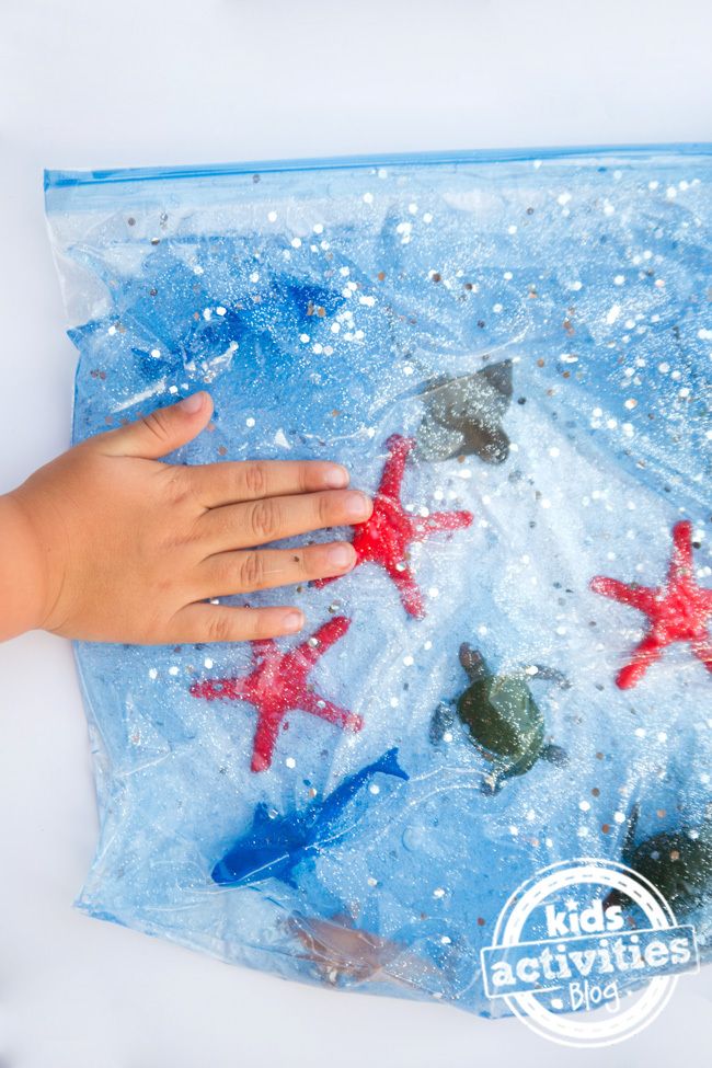 a child's hand on top of a plastic bag filled with sand and starfish