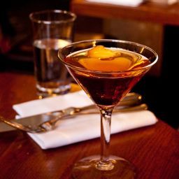 a glass filled with liquid sitting on top of a wooden table next to silverware