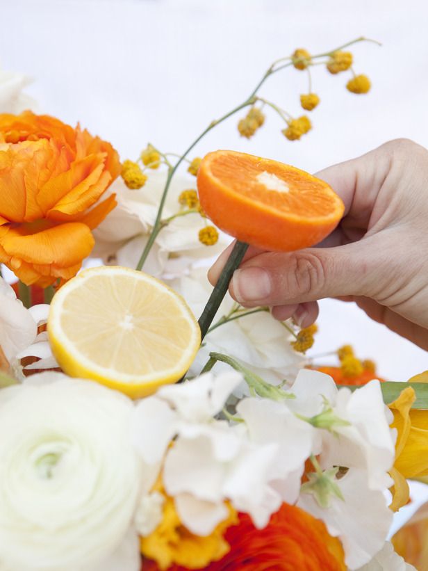 a person is holding an orange slice in front of a bouquet of flowers and peonies