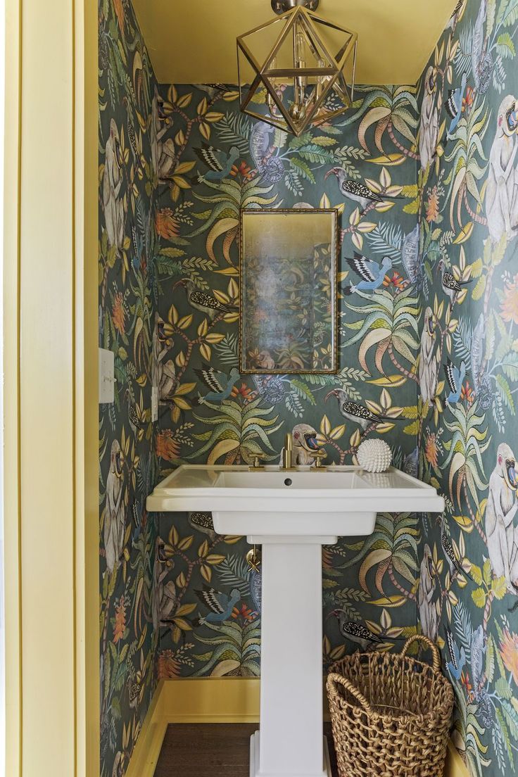 a bathroom with wallpaper and a pedestal sink in the corner next to a basket