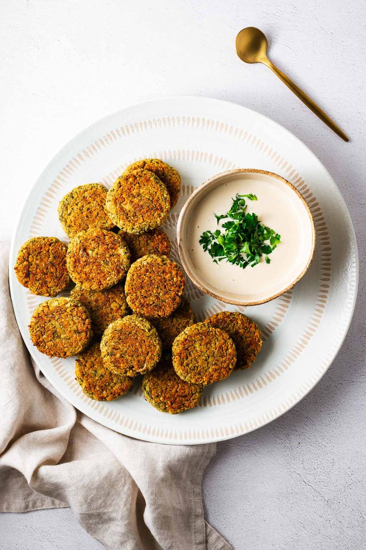 a white plate topped with crab cakes next to a small bowl of ranch dressing and a gold spoon