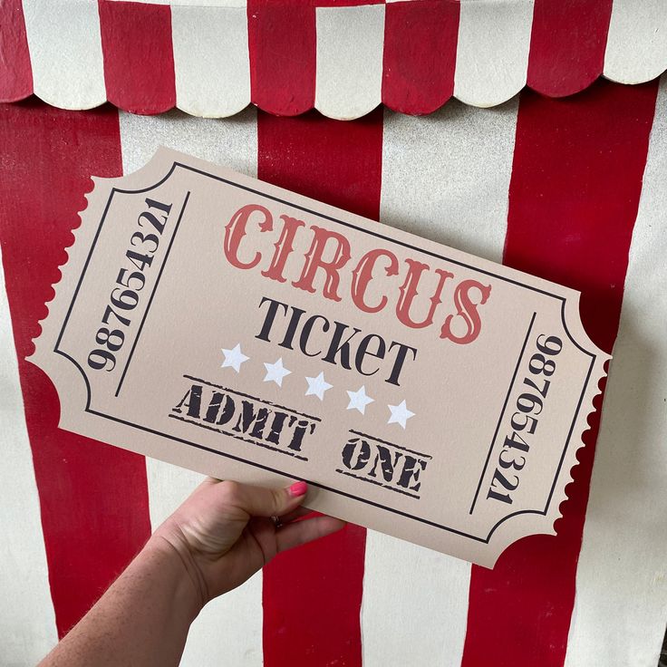 a person holding up a circus ticket in front of a red and white striped tent