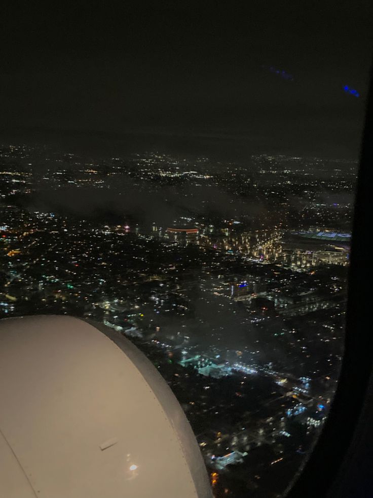 the view from an airplane window at night with city lights in the distance and fog on the ground