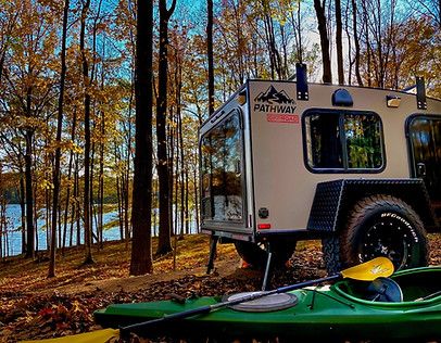 a green kayak sitting in the woods next to a camper