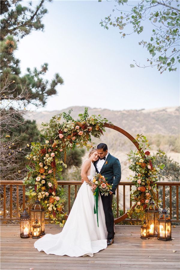 a bride and groom standing in front of an arch decorated with flowers, candles and greenery