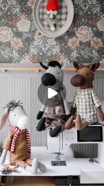 three stuffed animals sitting on top of a table next to a sewing machine and monitor