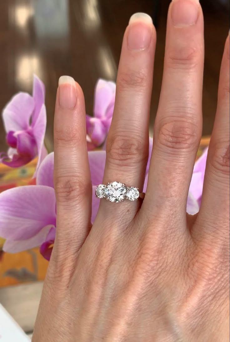 a woman's hand with a three stone ring on her finger and purple flowers in the background