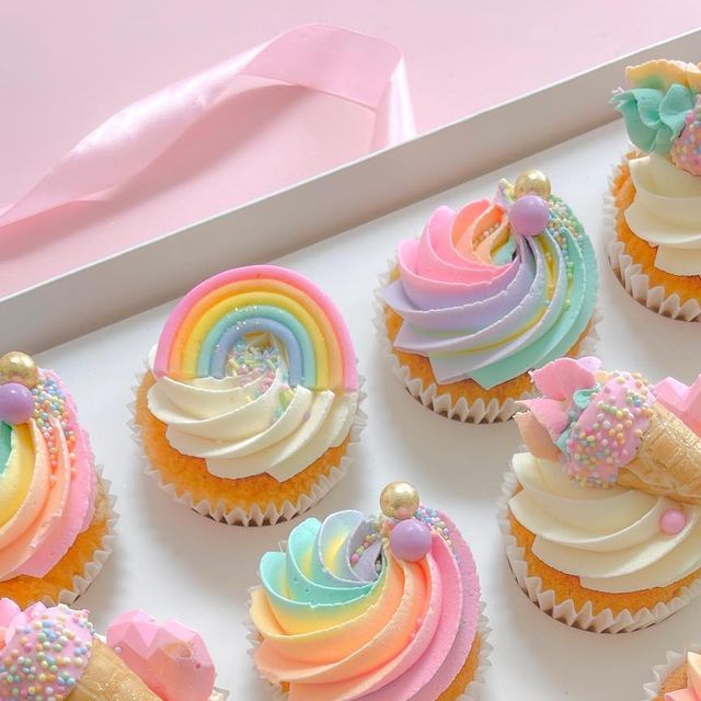 cupcakes decorated with rainbow icing and sprinkles in a box