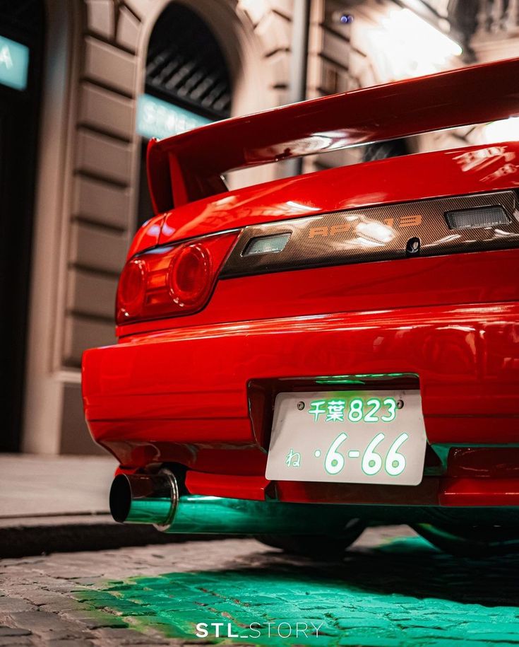 the back end of a red car parked in front of a building