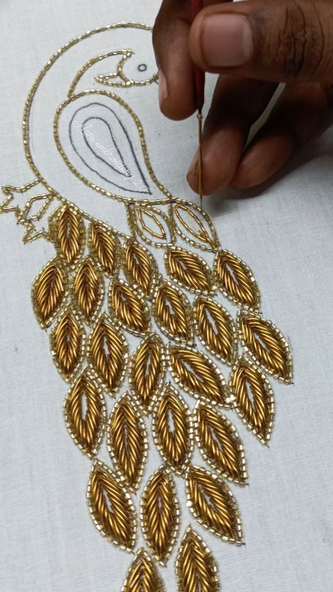 someone is working on an embroidered design with gold thread and beadwork in the shape of a peacock