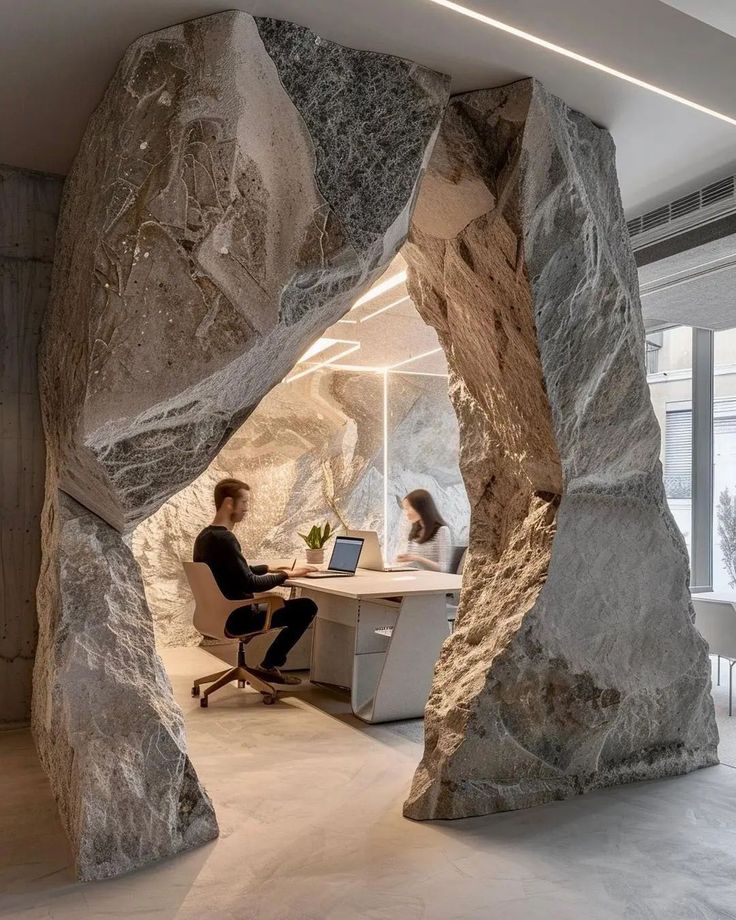 two people sitting at a desk in an office with large rocks on the walls and floor