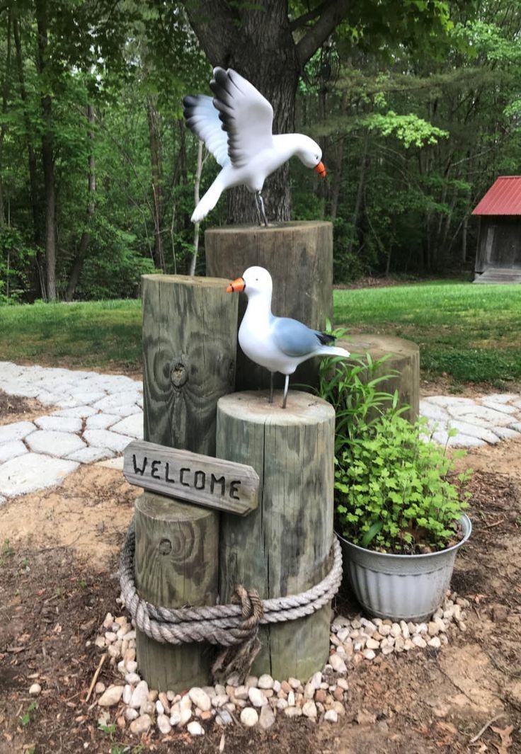 two seagulls sitting on top of wooden post with welcome sign and potted plants