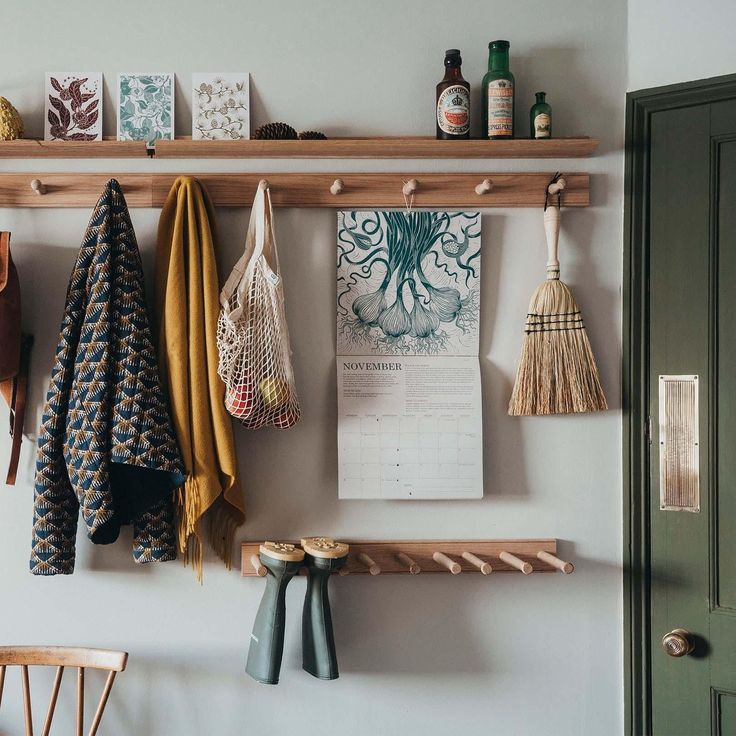 several coats hanging on the wall in front of a green door and wooden shelf with various items